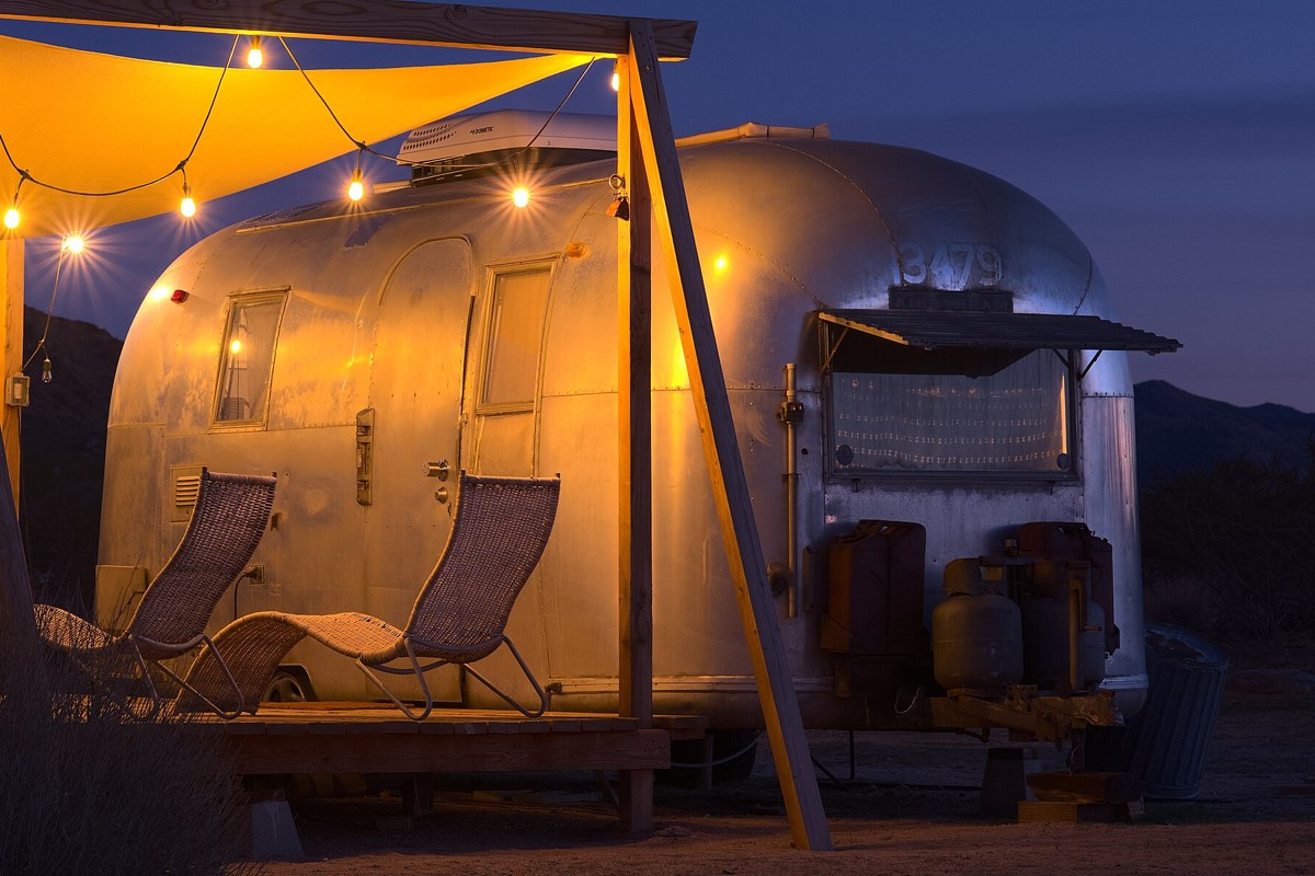 A vintage Airstream travel trailer lit by string lights at dusk in Joshua Tree